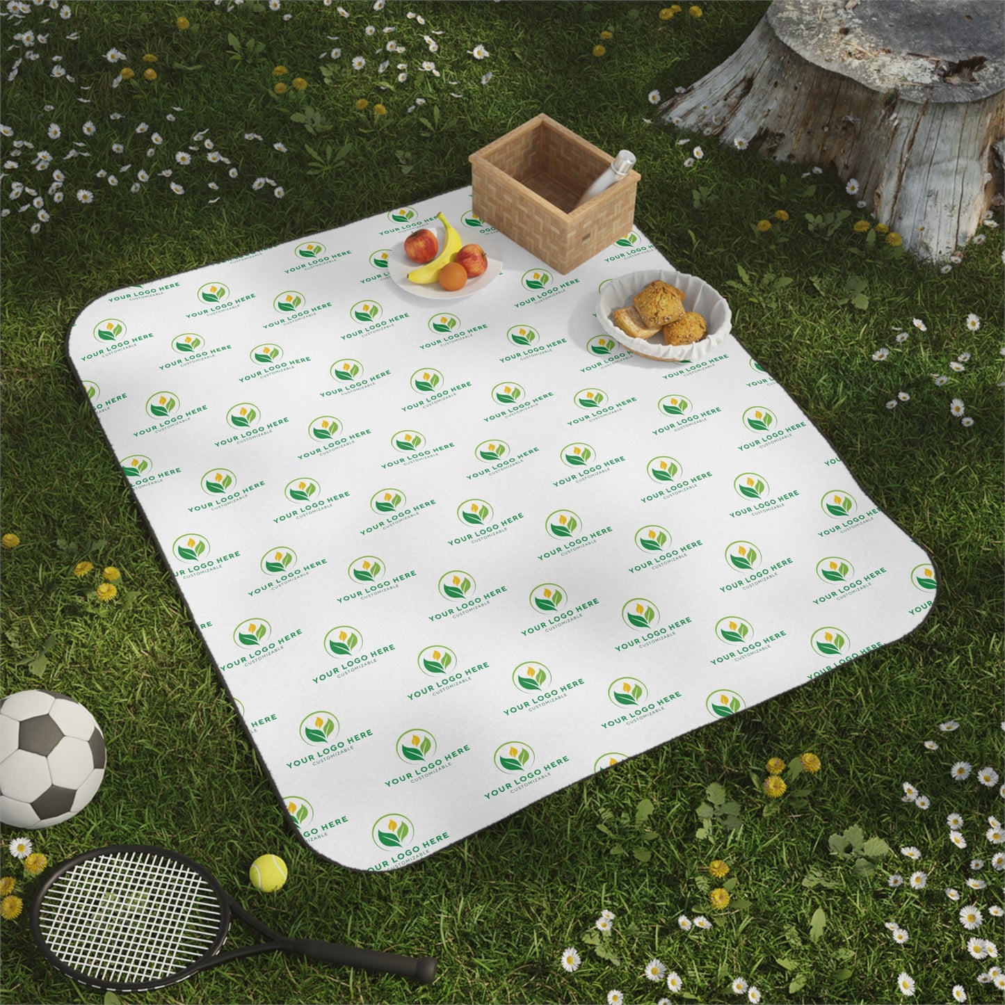 Picnic blanket with a brand logo on grass with a soccer ball and tennis racket.