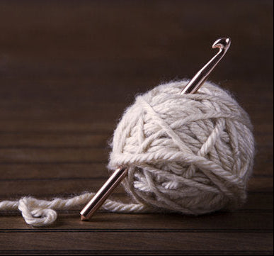 Ball of white yarn with a crochet hook on a wooden surface