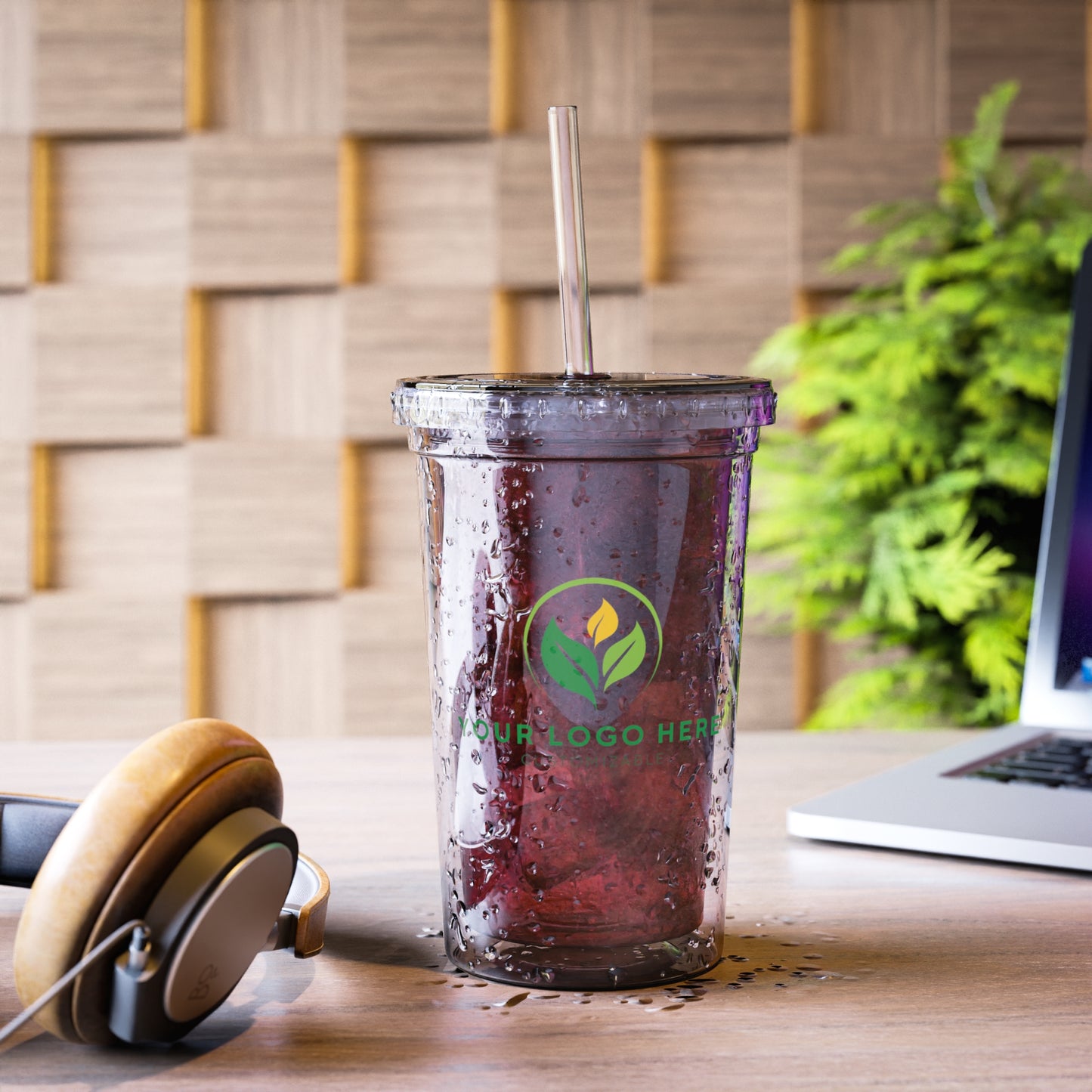 Cold brew coffee in a tumbler with a straw on a desk, next to headphones and a laptop.