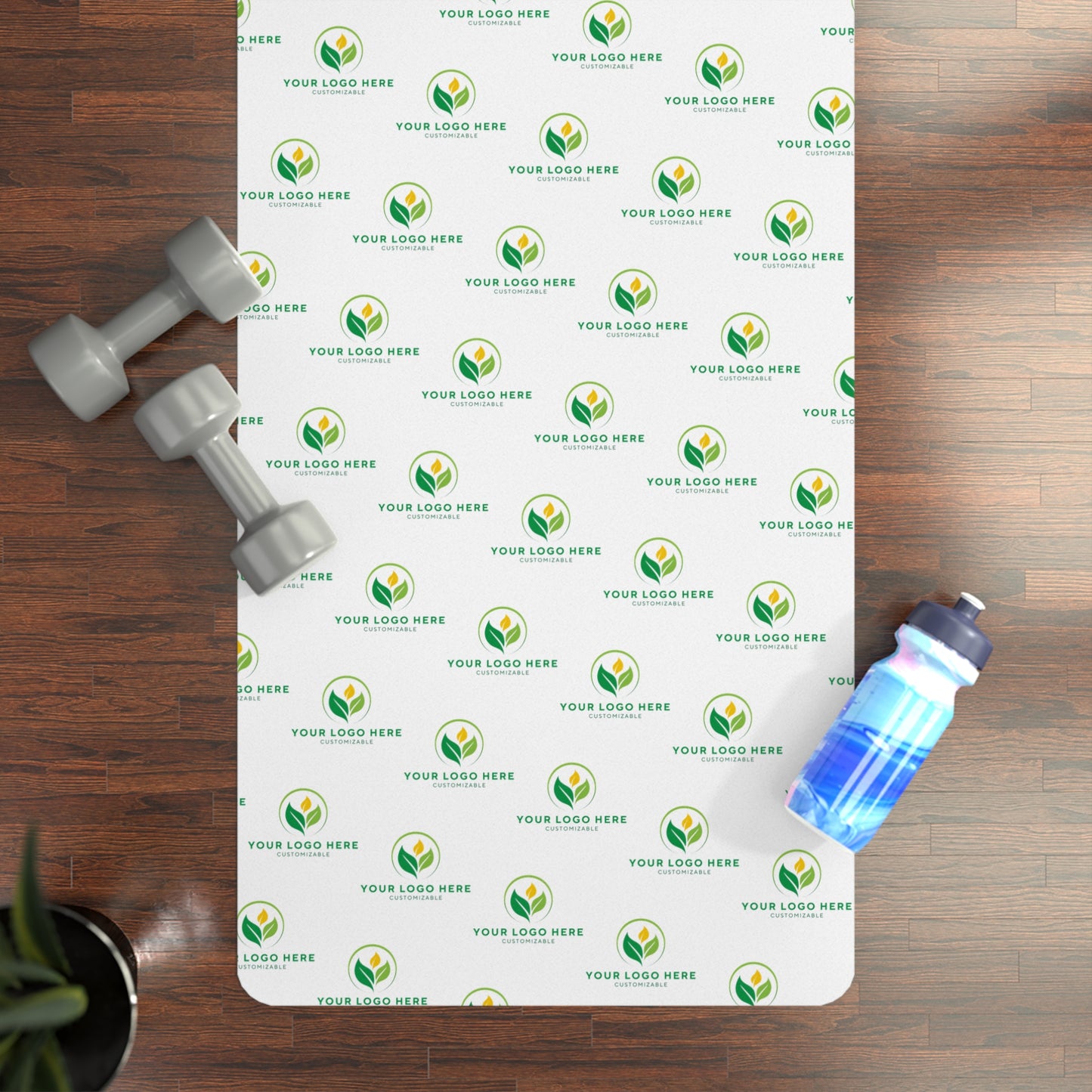 Personalized yoga mat with brand logo, dumbbells, and water bottle on a wooden floor.