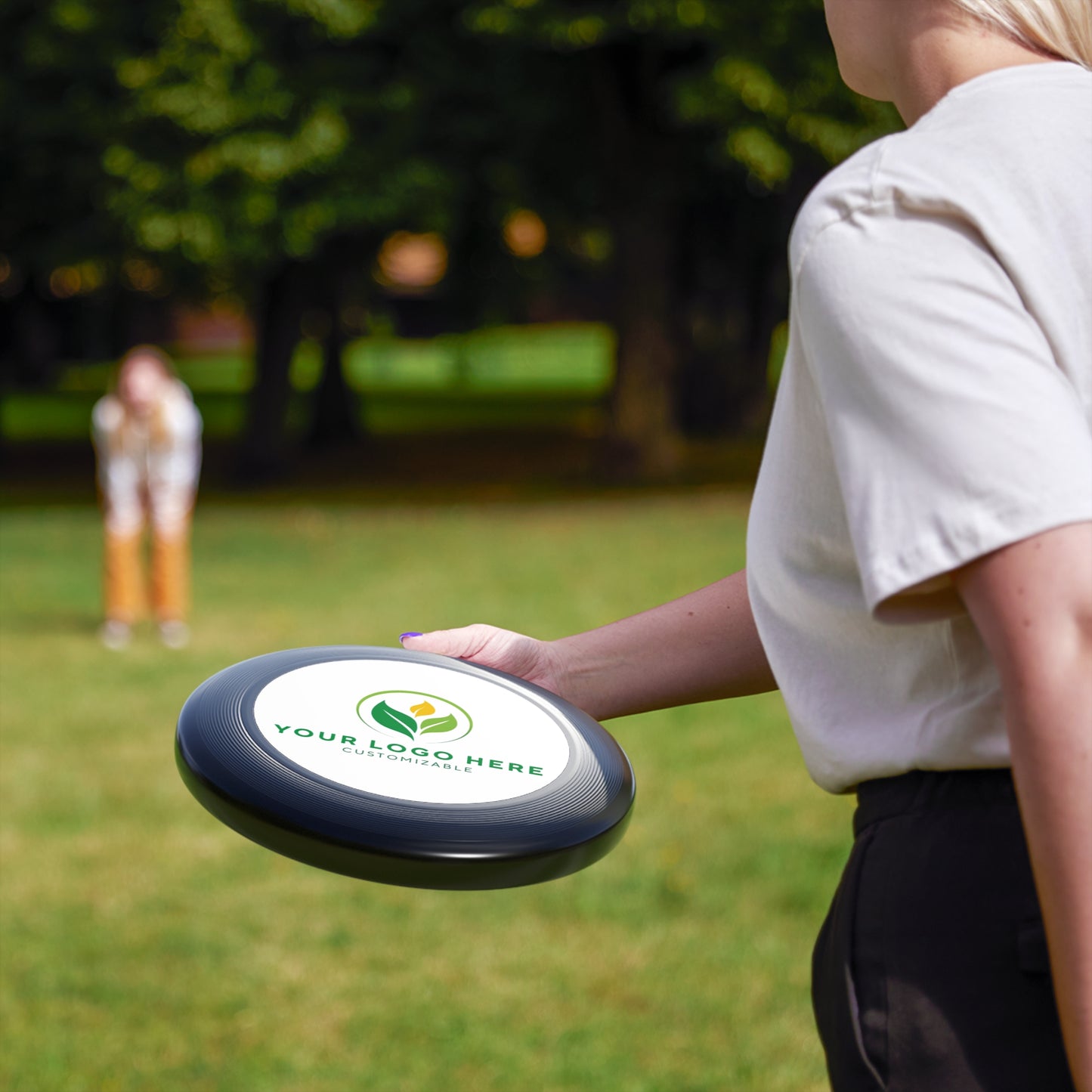Person holding a frisbee with a logo in a park setting