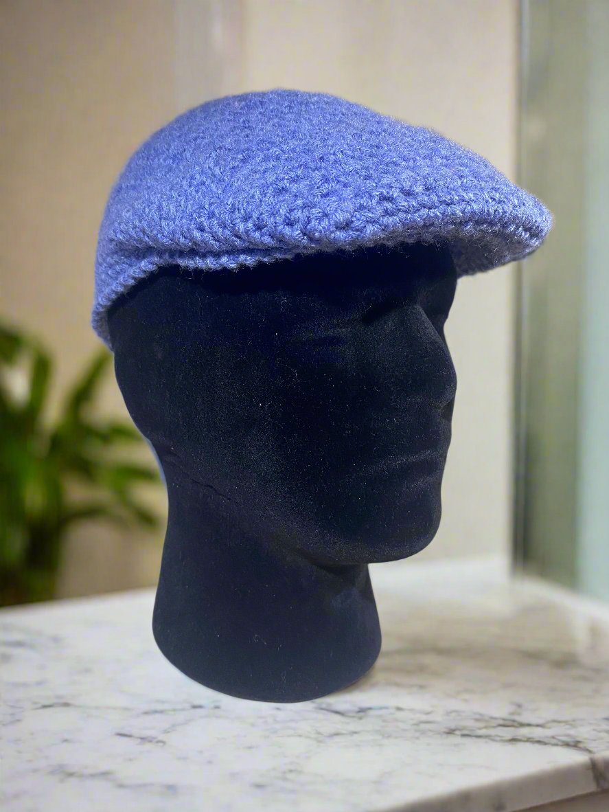 A beige crochet newsboy cap displayed on a mannequin head against a marble background.