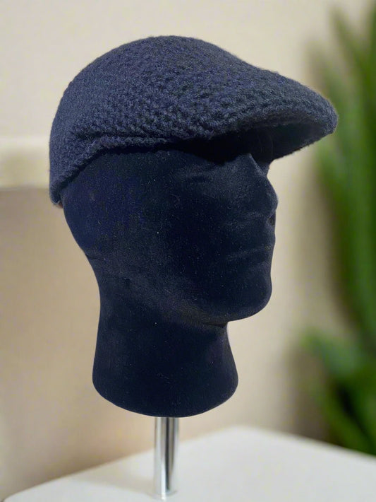 A beige crochet newsboy cap displayed on a mannequin head against a marble background.