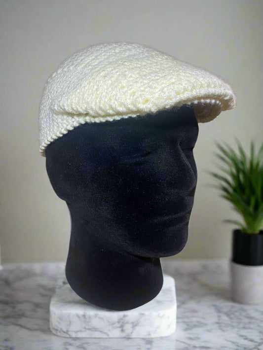 A white crochet newsboy cap displayed on a mannequin head against a marble background.