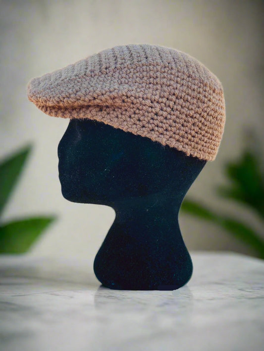 A beige crochet newsboy cap displayed on a mannequin head against a marble background.