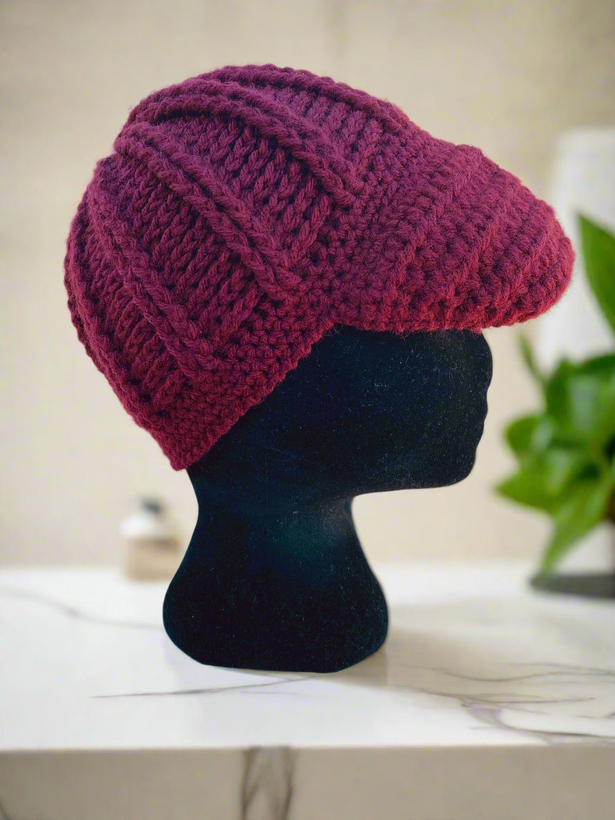 A handcrafted crochet hat in wine red with a flower design, displayed on a mannequin head, set against a natural background.