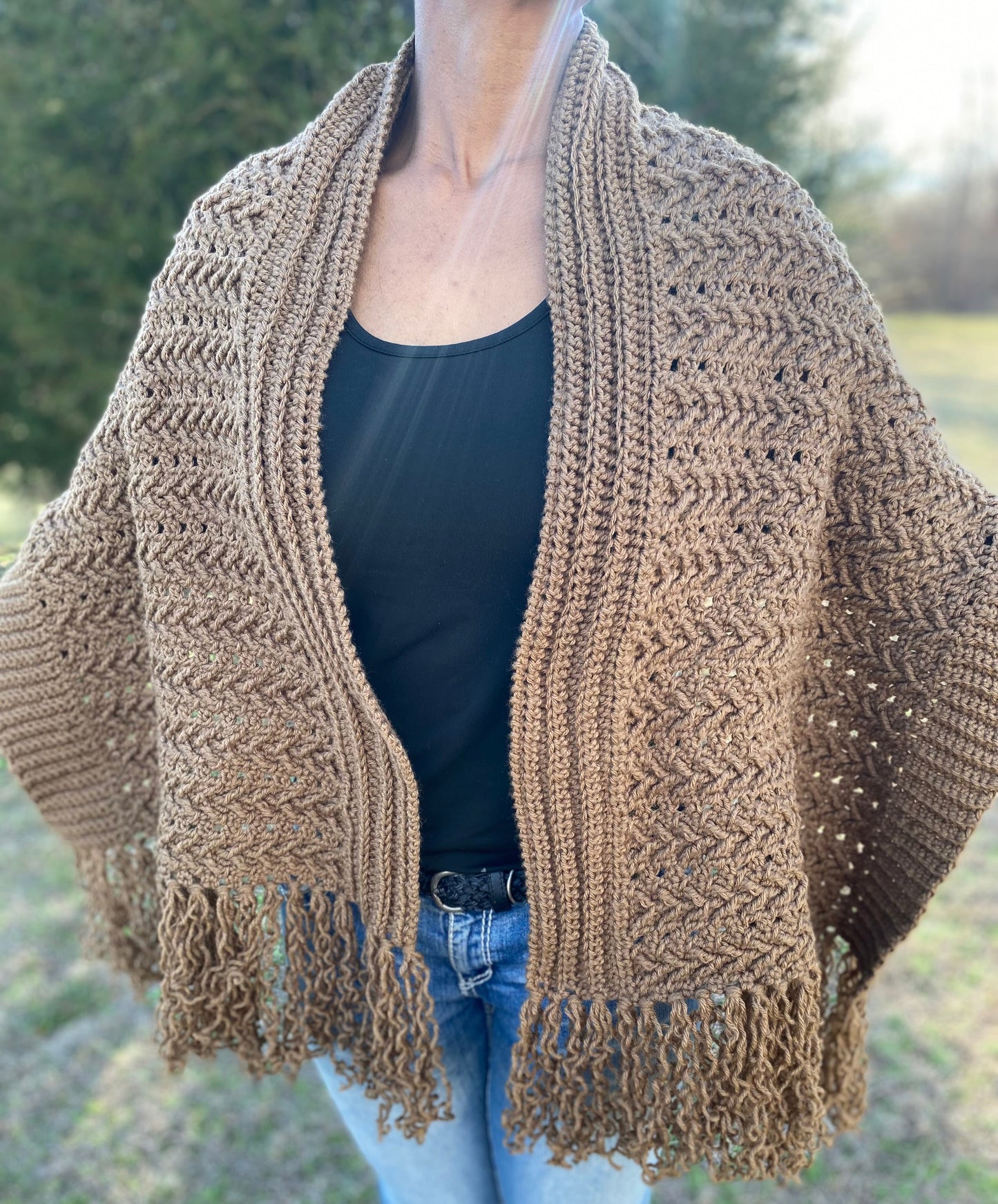 Person wearing a brown crochet shawl over a black top and blue jeans outdoors.