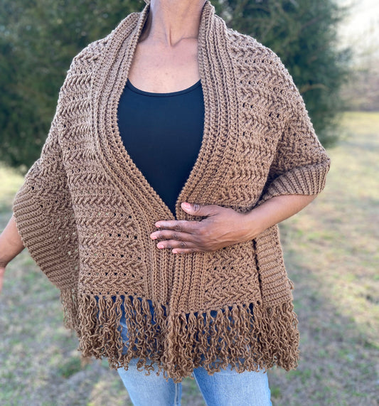 Person wearing a brown crochet poncho with fringe in an outdoor setting