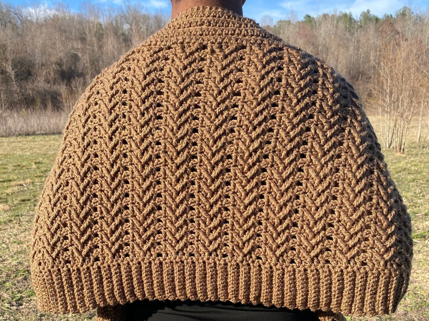 Brown crochet shawl worn by a person in an outdoor setting with trees and grass.