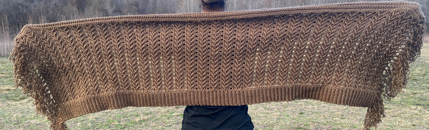 Brown crochet shawl held by a person in an outdoor setting