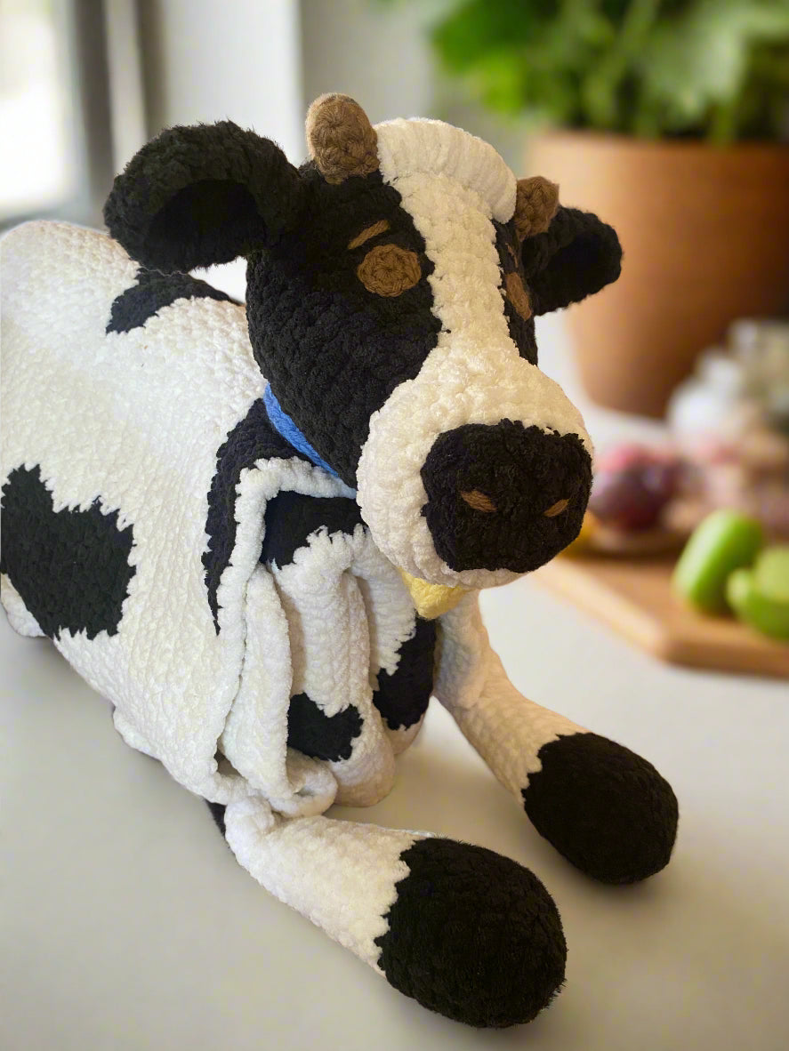 Crocheted cow blanket with black and white pattern on a soft surface