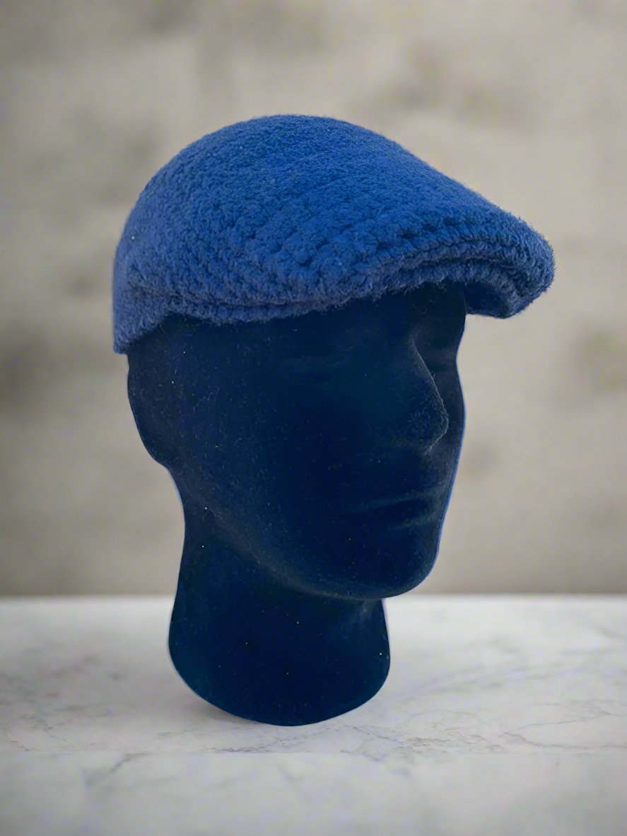A blue crochet newsboy cap displayed on a mannequin head against a marble background.