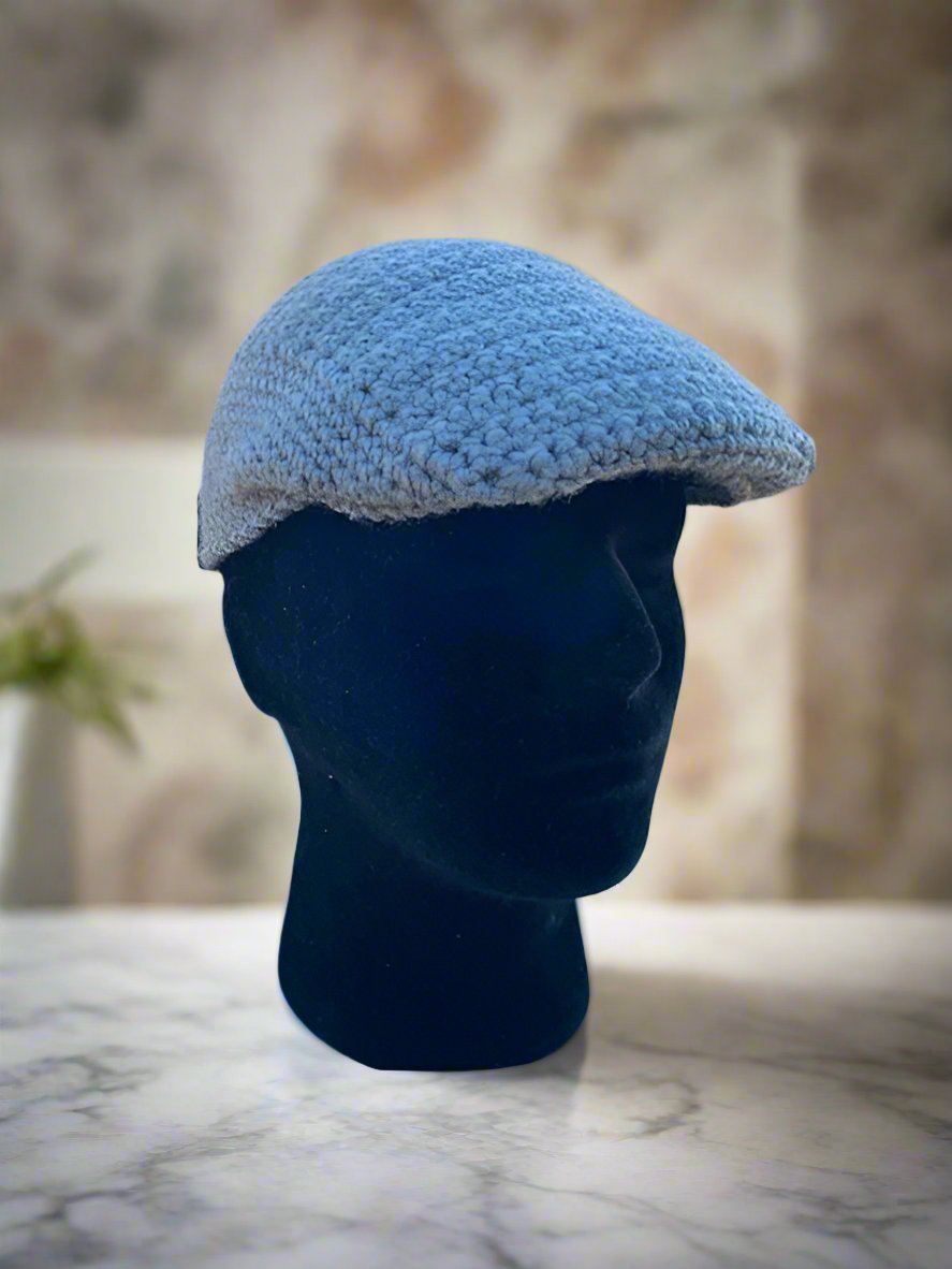 A light blue crochet newsboy cap displayed on a mannequin head against a marble background.