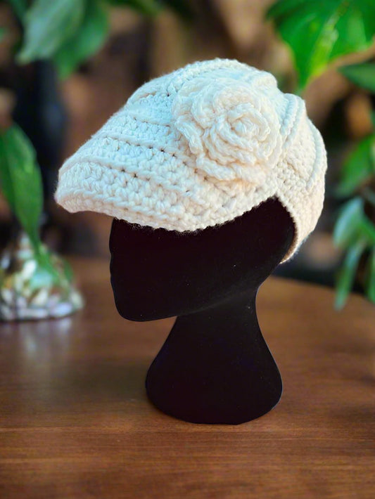A handcrafted crochet hat in white with a flower design, displayed on a mannequin head, set against a natural background.