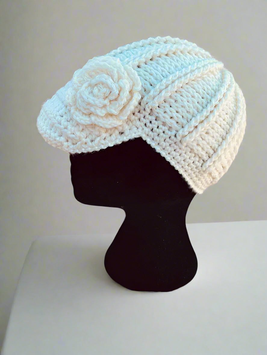 A handcrafted crochet hat in white with a flower design, displayed on a mannequin head, set against a natural background.