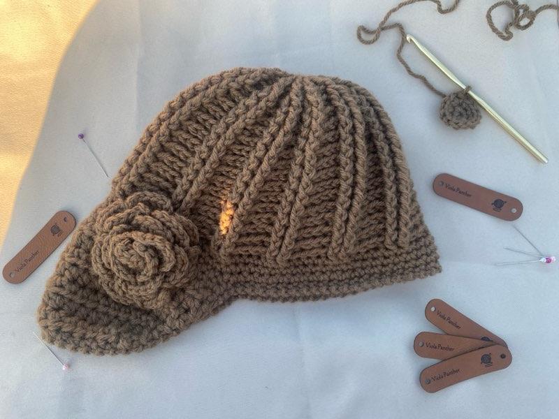 A handcrafted crochet hat in brown with a flower design, displayed on a white background