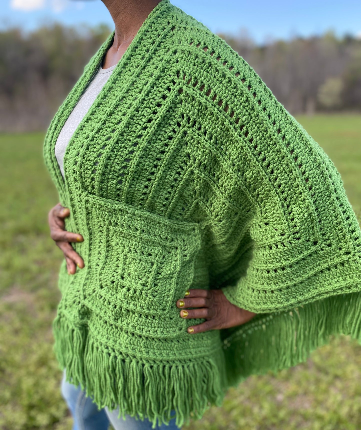 Person wearing a green crochet poncho in an outdoor setting