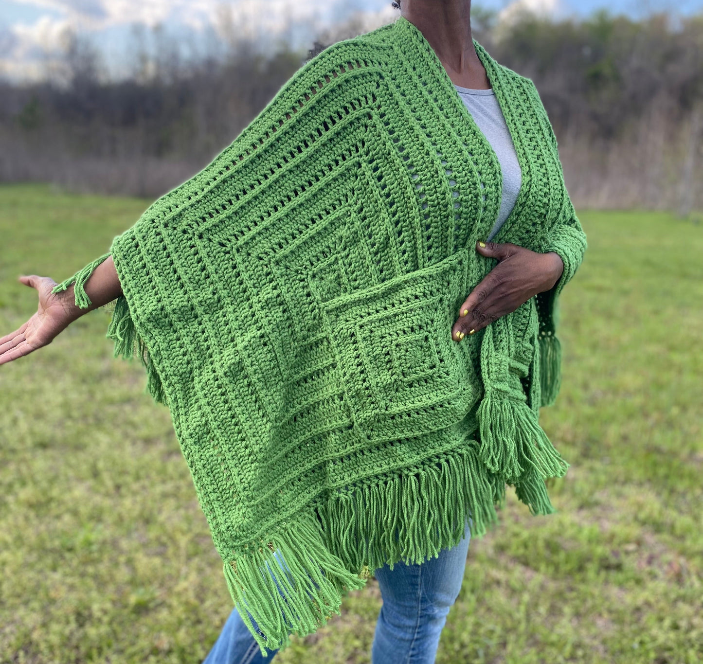 Person wearing a green crocheted poncho in an outdoor setting