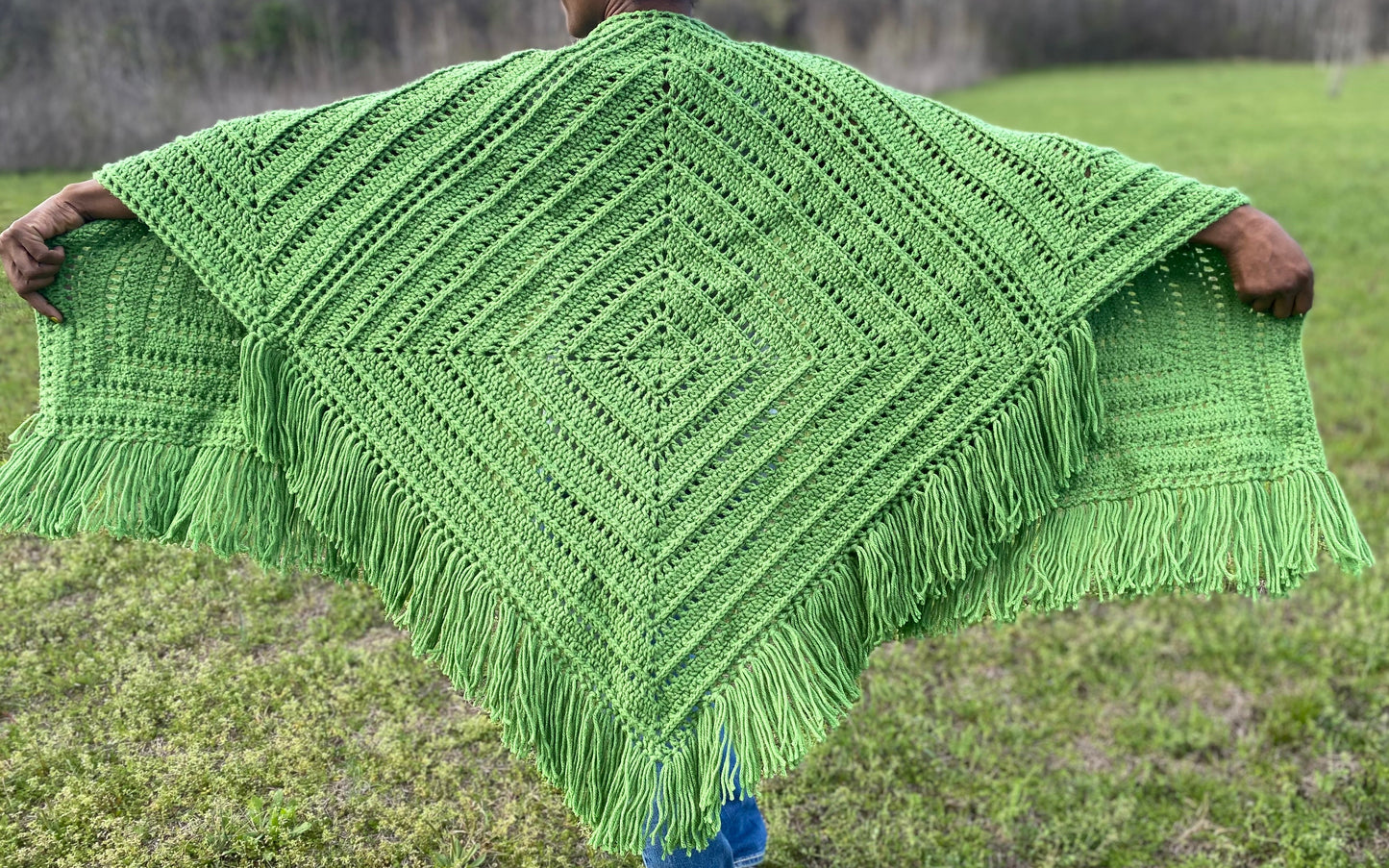 Person wearing a green crocheted shawl in an outdoor setting