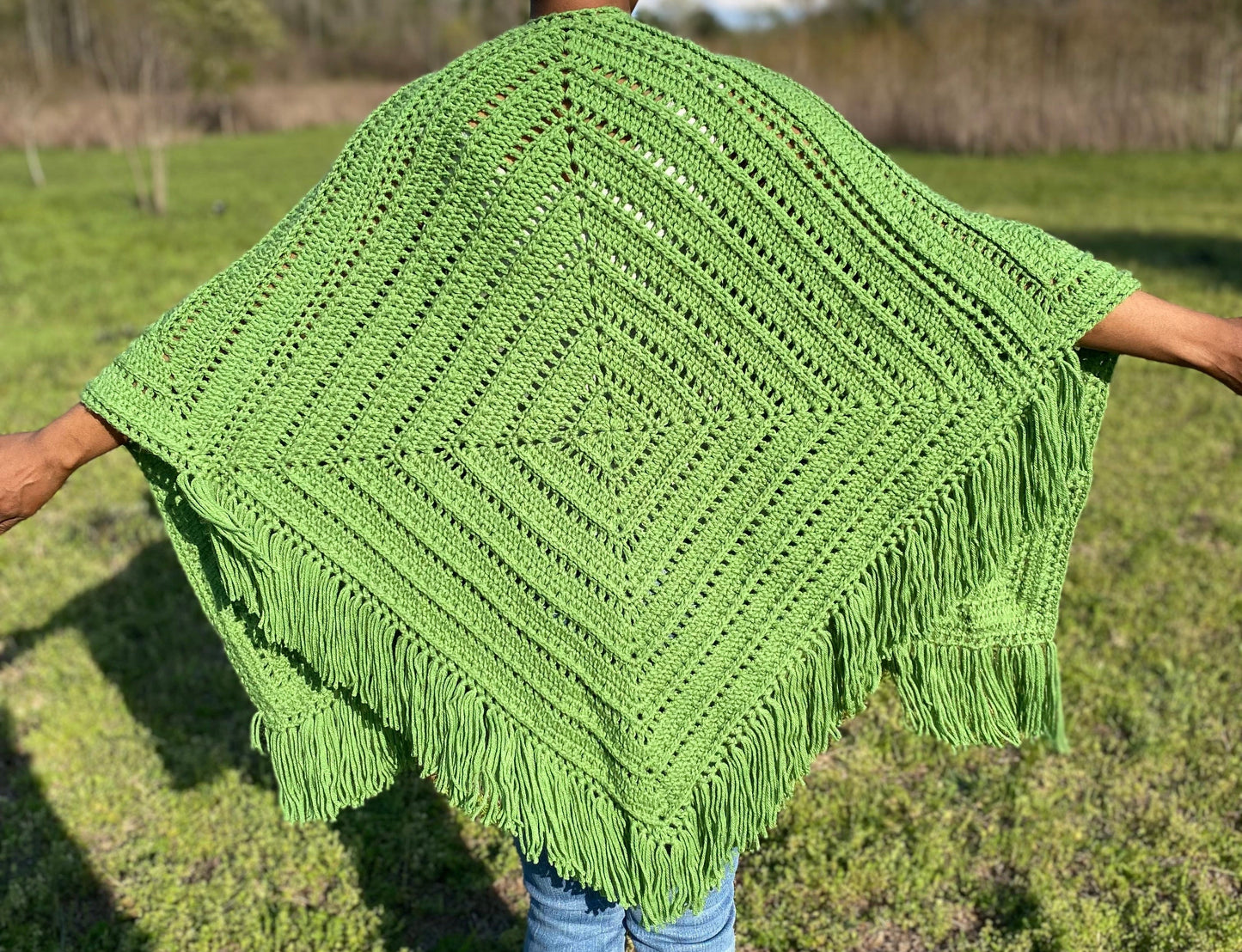 Green crocheted shawl with tassels held by a person in an outdoor setting
