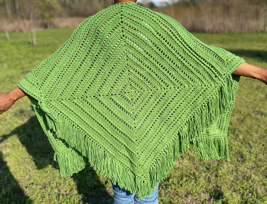 Green crocheted shawl with tassels held by a person in an outdoor setting
