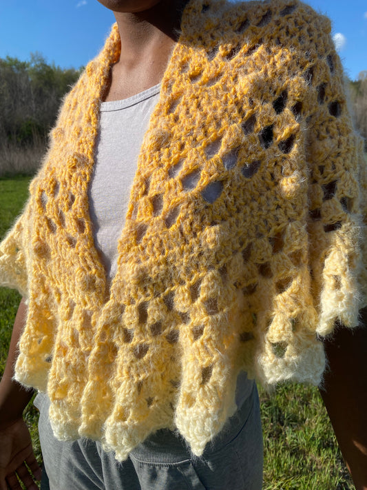 Person wearing a yellow crochet shawl in a field.