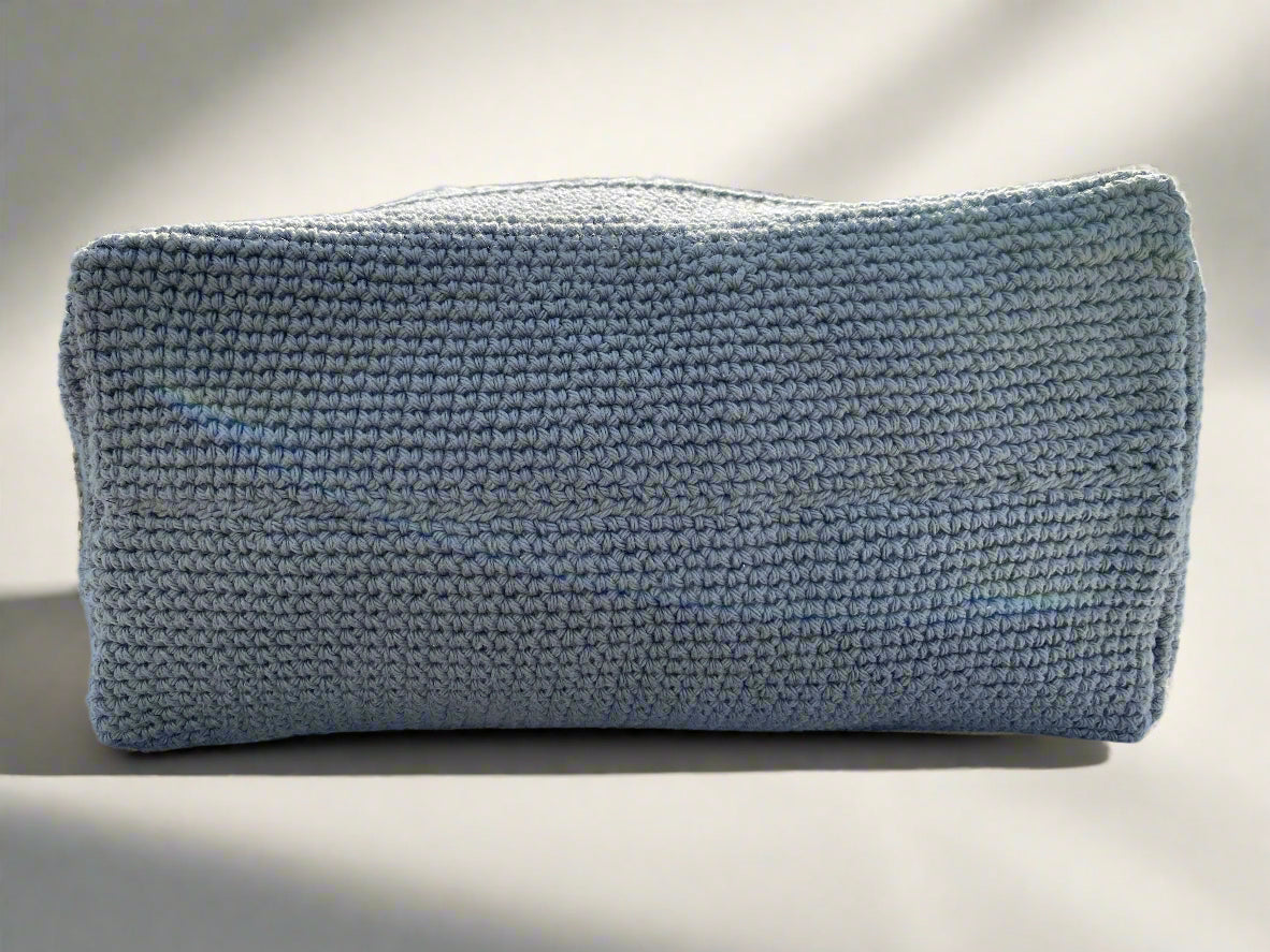 A crochet tote bag with two-tone design, featuring grey and white colors with braided handles and a faux leather tag.