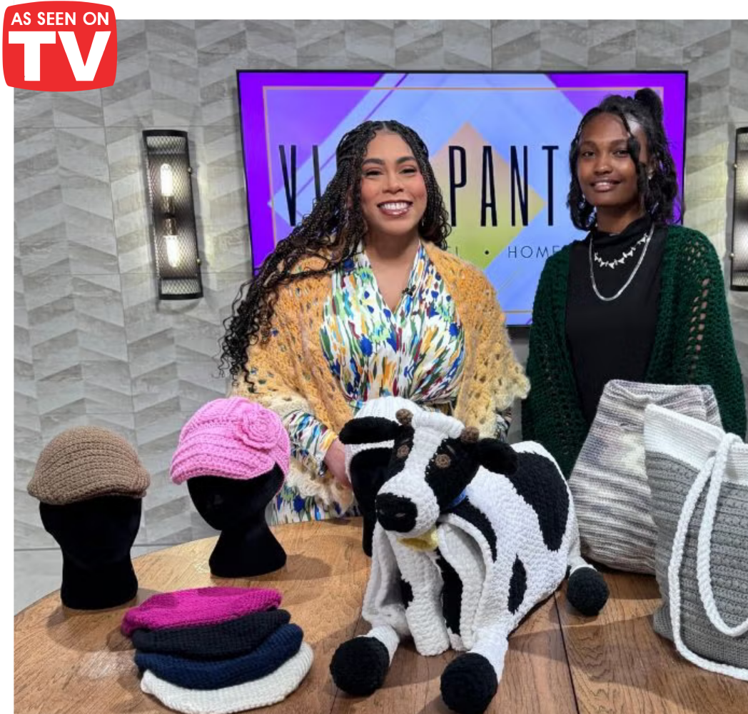 Two women with a cow, bags, and a mannequin with hats on a table, with a TV screen in the background displaying 'As Seen on TV'.