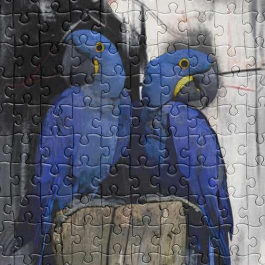 Close up of a jigsaw puzzle depicting two blue hyacinth macaws perched on a wooden stump with a custom name label, surrounded by a blurred background.