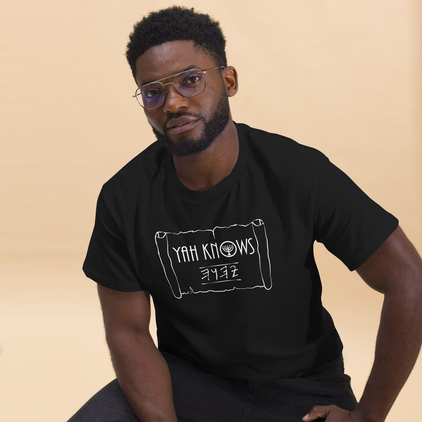 A person wearing a black unisex crew neck t-shirt with the text 'YAH Knows' printed in white on the front.