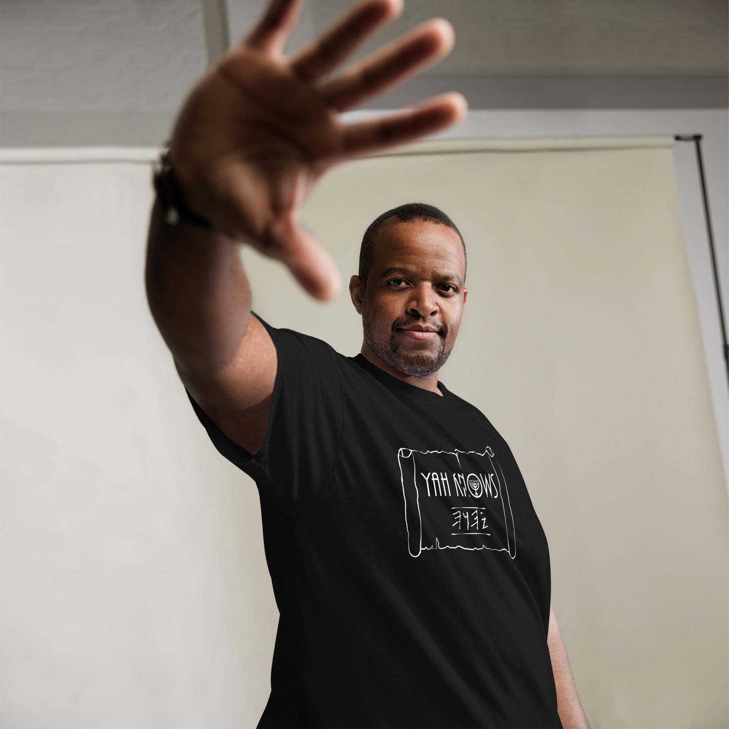 A person wearing a black unisex crew neck t-shirt with the text 'YAH Knows' printed in white on the front.
