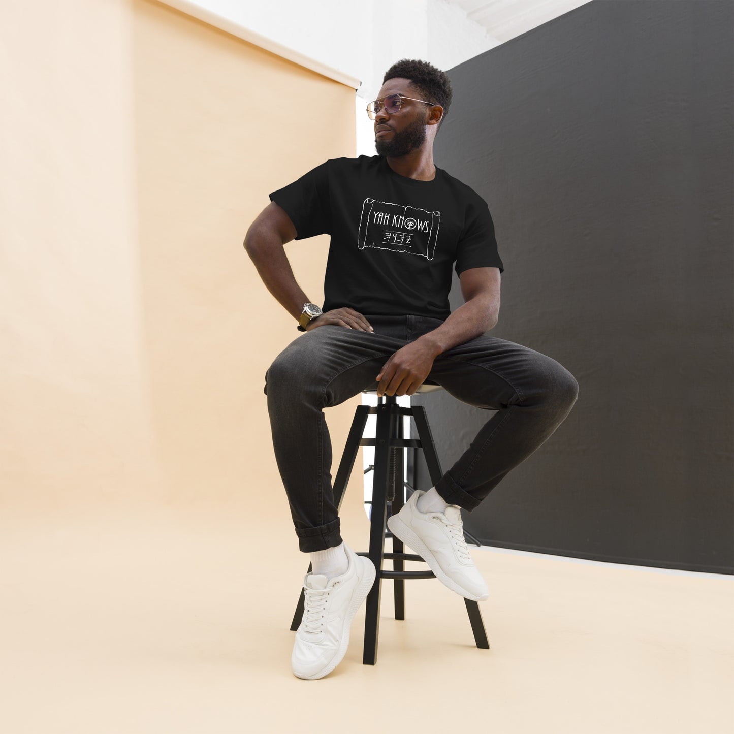 A person wearing a black unisex crew neck t-shirt with the text 'YAH Knows' printed in white on the front.