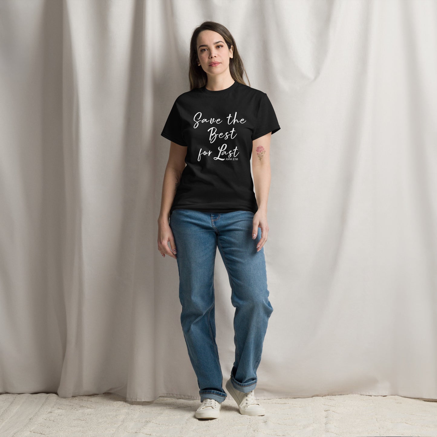 Person wearing a black t-shirt with text and blue jeans standing against a plain background