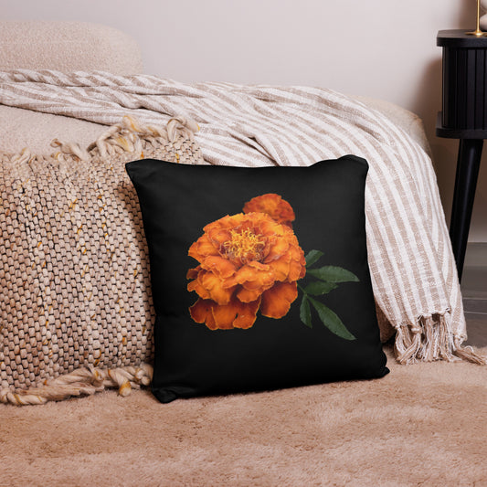 A square throw pillow with an image of an orange flower on a black background, placed on a sofa next to a textured blanket.