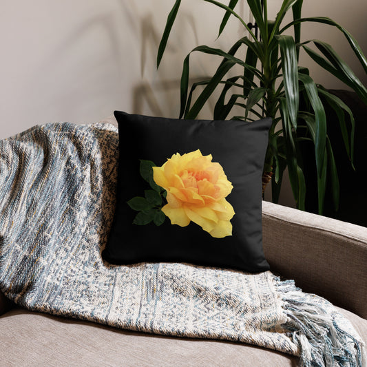 A rectangular throw pillow with a hidden zipper, featuring a printed yellow flower design on a black case, placed on a sofa beside a grey blanket and a potted plant.