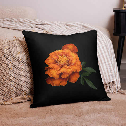 A square throw pillow with an image of an orange flower on a black background, placed on a sofa next to a textured blanket.