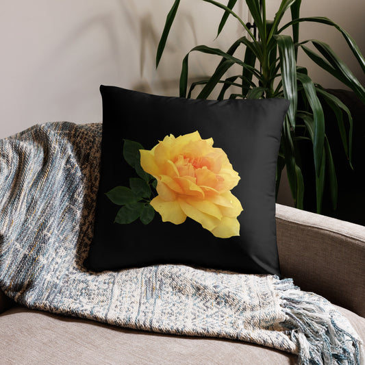 A black pillow with a yellow flower print, placed on a sofa next to a grey blanket and a green plant.