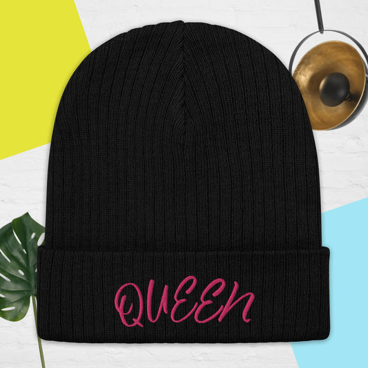 A black ribbed knit beanie with the word 'QUEEN' written in pink on the cuff.