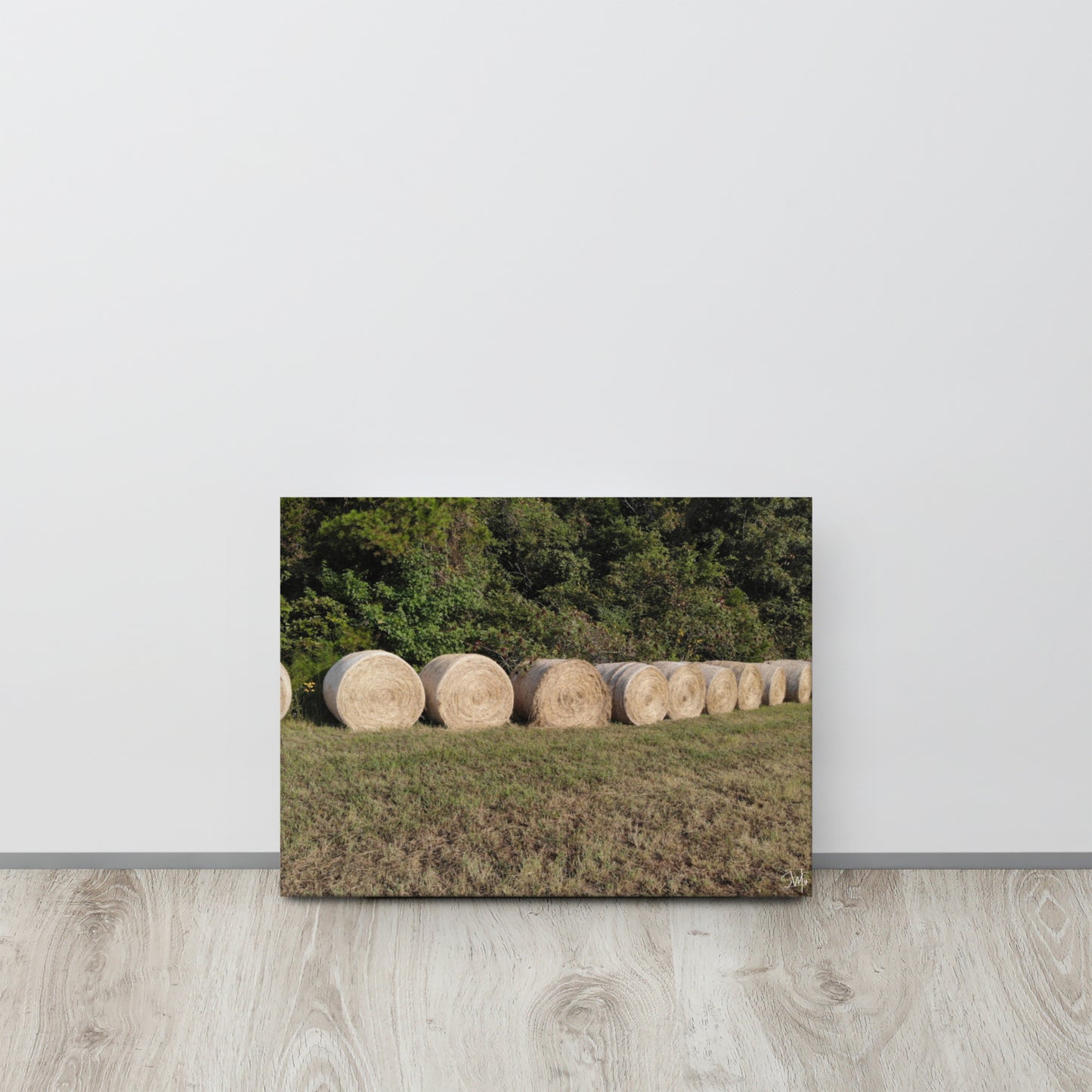 A canvas print featuring a rural landscape with a row of hay bales.