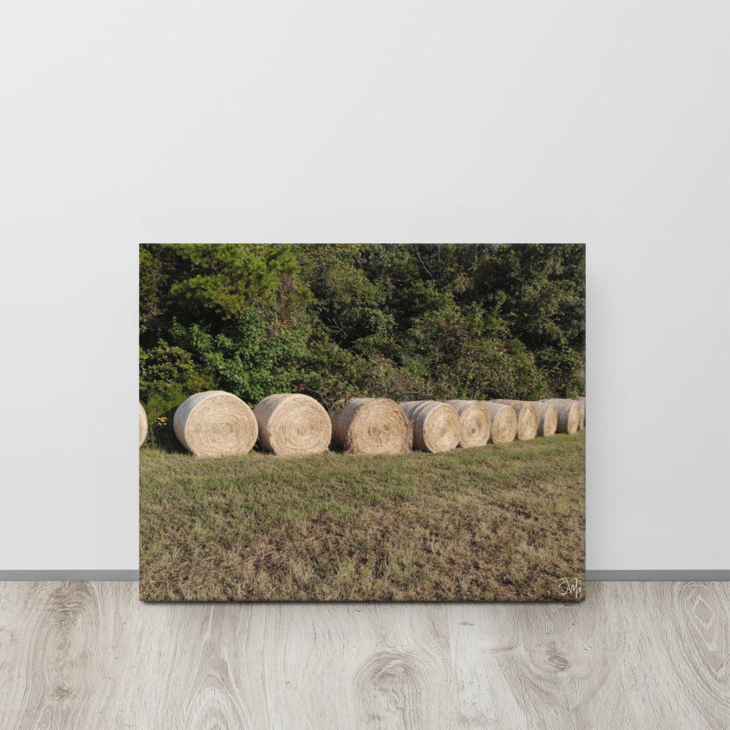 A canvas print featuring a rural landscape with a row of hay bales.
