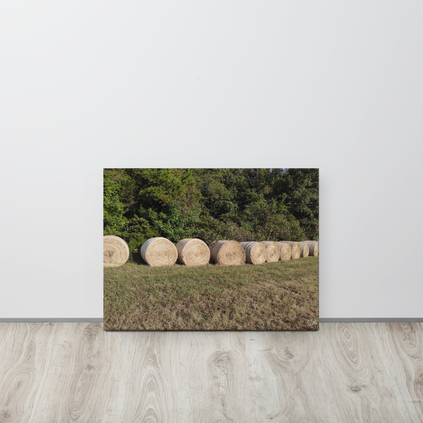 A canvas print featuring a rural landscape with a row of hay bales.