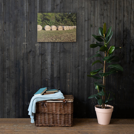 A canvas print featuring a field of hay bales under a clear sky, displayed on a white wall.
