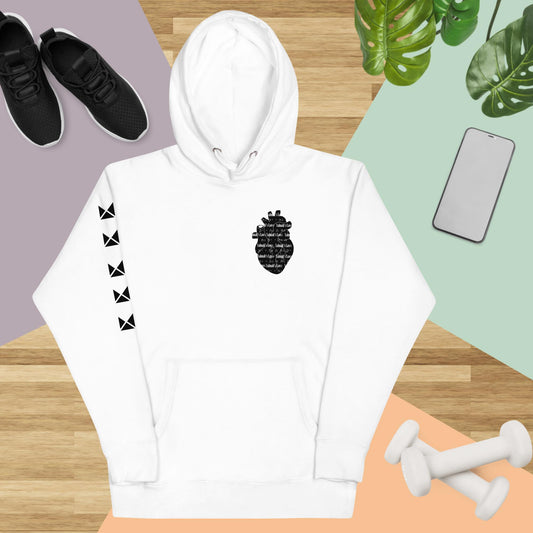 A white unisex hoodie with text design on the front, a pineapple and heart graphic, and a hood. Displayed on a flat surface with a black shoes, a potted plant, and exercise equipment in the background.