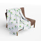 White blanket with green leaf logo draped over a brown chair on a white background