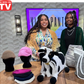 Two women with a cow, bags, and a mannequin with hats on a table, with a TV screen in the background displaying 'As Seen on TV'.